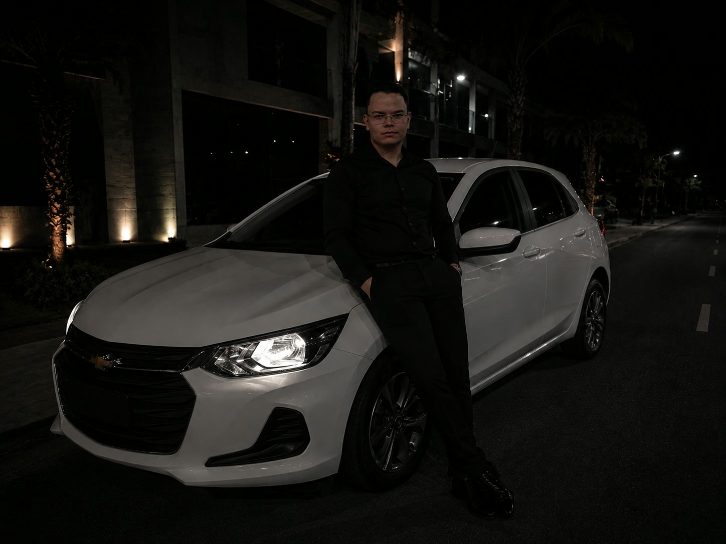 Motorista particular ao lado de carro branco em ambiente urbano à noite